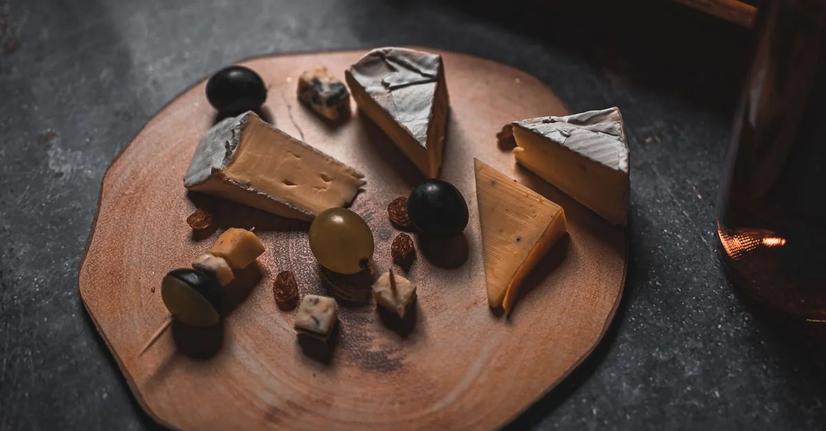 Un plateau de fromages rustique avec divers fromages, noix et raisins sur une planche en bois.