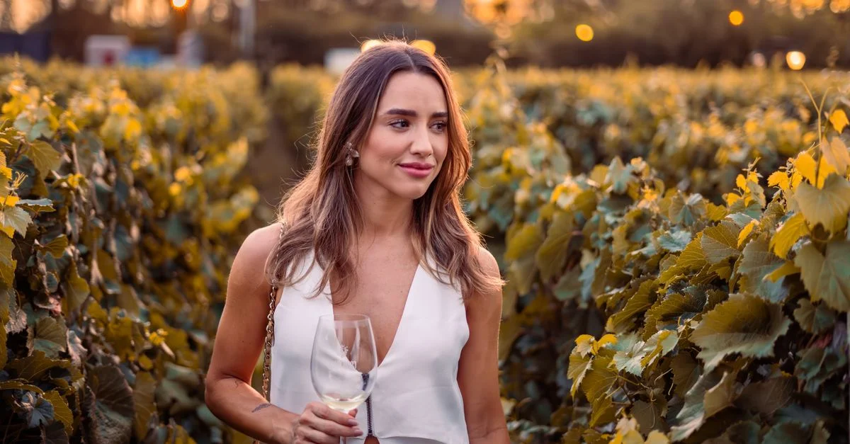 Une femme avec un verre de vin se promène à travers un vignoble luxuriant au coucher du soleil, profitant d'une soirée en plein air.