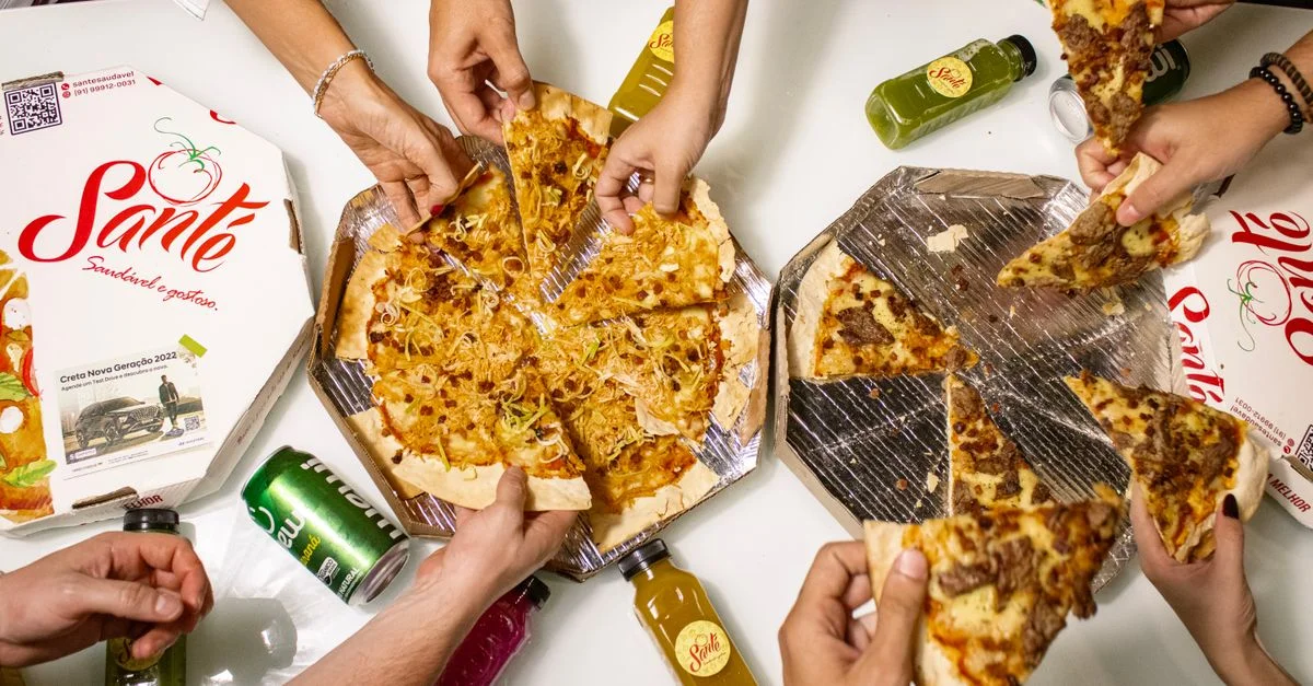 Vue de dessus d'amis partageant des tranches de pizza avec des boissons, parfait pour une ambiance de repas décontractée.