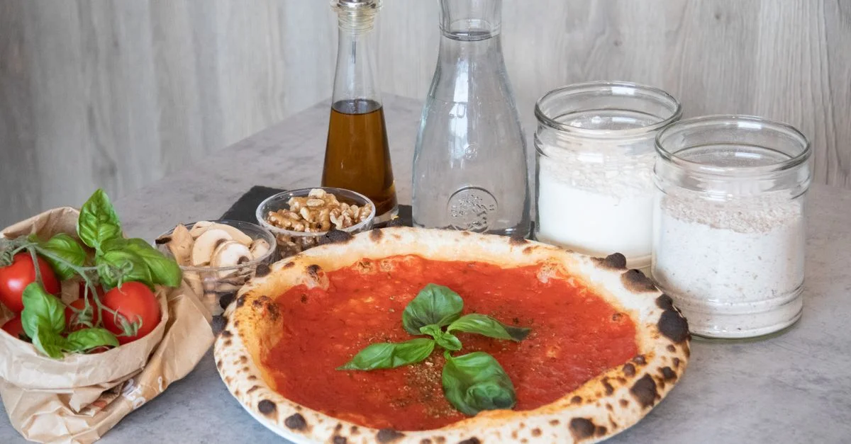 Pizza fraîchement cuite avec des ingrédients italiens classiques disposés sur une surface grise.