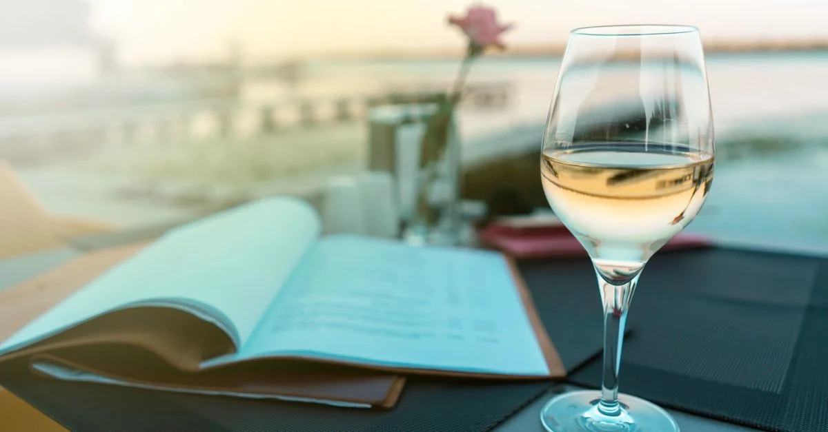Un verre de vin blanc sur une table au bord du lac pendant le coucher de soleil, créant une atmosphère de dîner sereine.