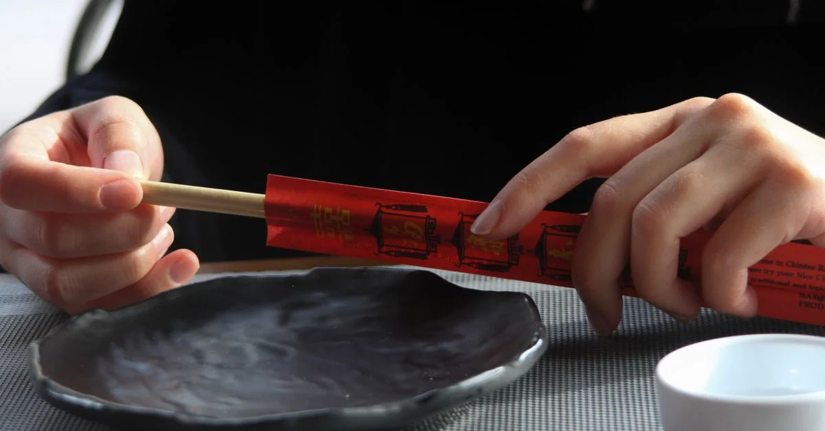 Gros plan sur des mains tenant des baguettes au-dessus d'une assiette vide, parfait pour des thèmes de cuisine asiatique.