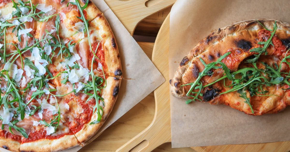 Des pizzas fraîchement cuites garnies de prosciutto, de roquette et de fromage, servies sur des planches en bois.