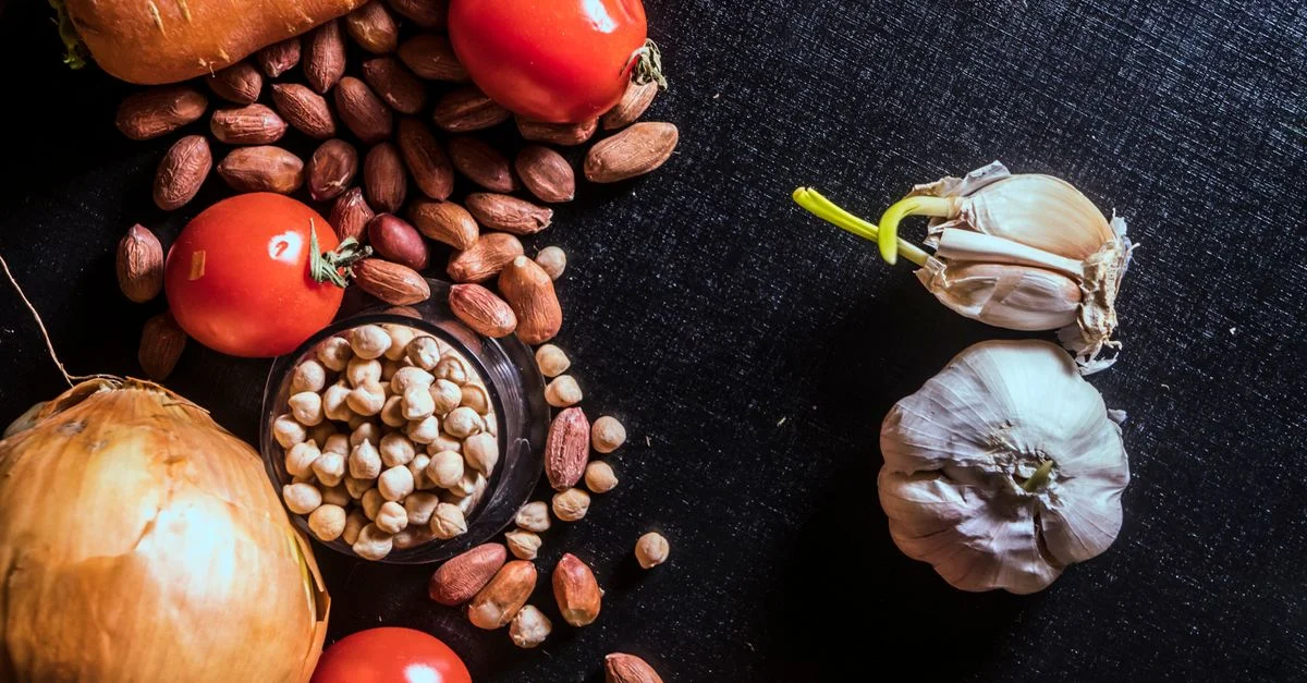 Vue de dessus de légumes frais et de noix disposés sur une surface sombre, mettant en valeur des ingrédients bruts.