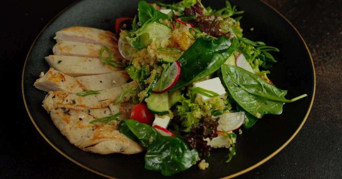Une salade vibrante avec du poulet grillé, du quinoa et des légumes frais sur une assiette noire.