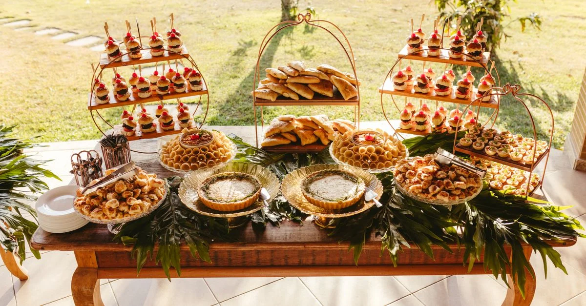 Une table de desserts magnifiquement agencée en extérieur avec diverses pâtisseries et douceurs dans un cadre de jardin sous la lumière du soleil.