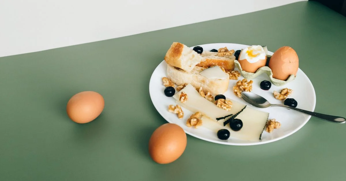 Assiette de fromage, œufs durs, pain, noix et myrtilles pour un petit-déjeuner copieux.