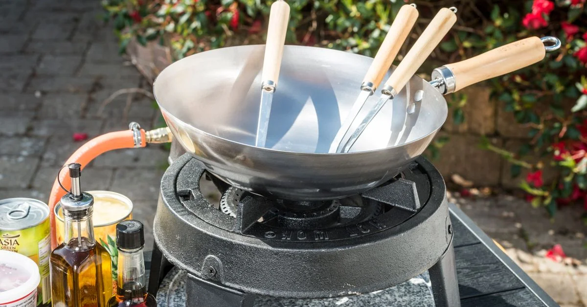 Une station de cuisine extérieure avec un wok, des ustensiles et des ingrédients de cuisson.