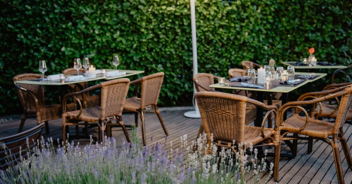 Terrasse de restaurant extérieure accueillante avec des chaises en rotin, des tables et de riches haies vertes.