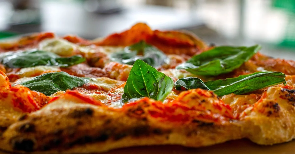 Gros plan sur des feuilles de basilic frais sur une pizza italienne classique avec du fromage fondu et de la sauce tomate.