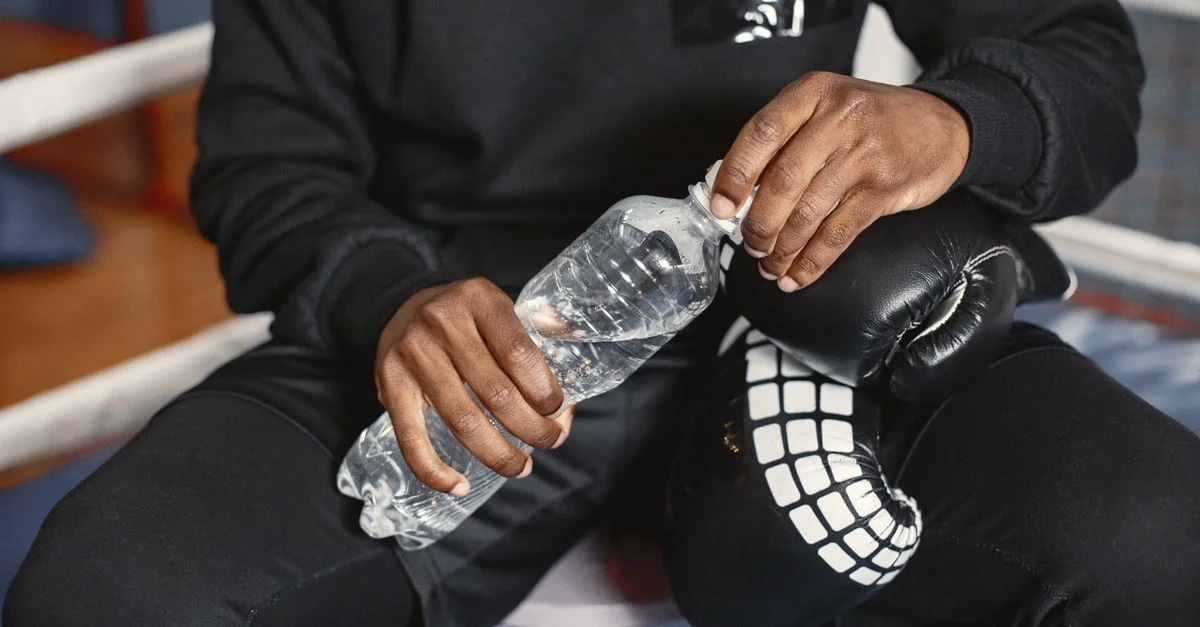 Un boxeur en tenue noire tenant une bouteille d'eau pendant une pause à l'intérieur.