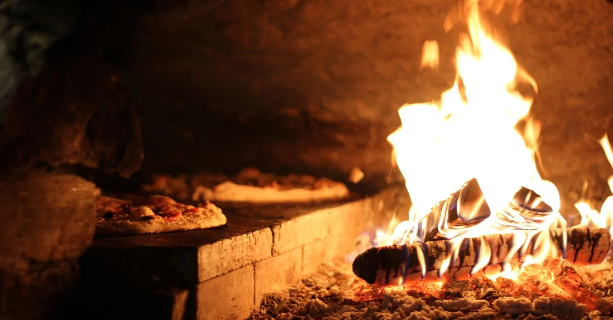 Un gros plan d'un four en bois rustique avec des pizzas près des flammes vives.