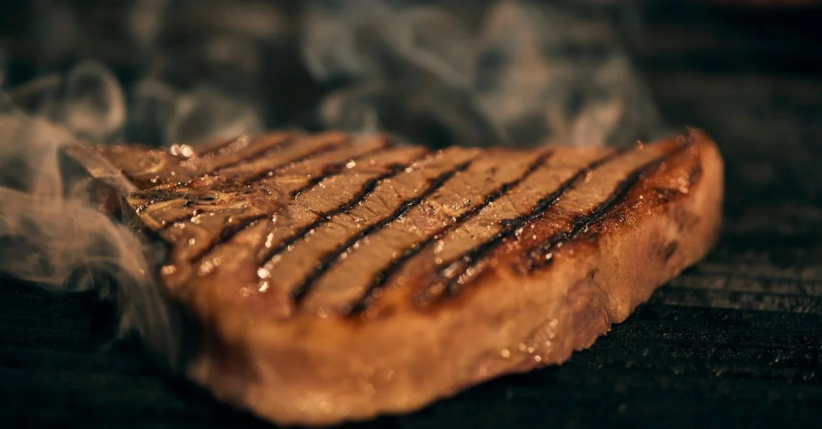 Gros plan d'un steak juteux grillé sur un barbecue avec un fond fumé.