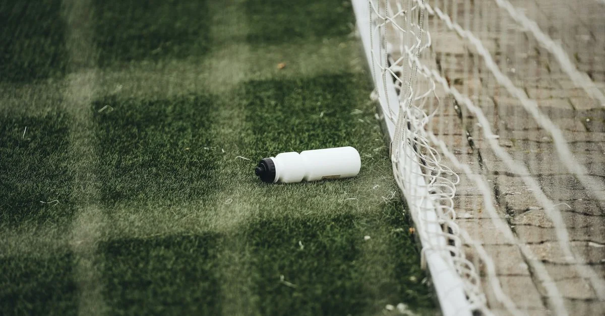 Une bouteille d'eau blanche sur un terrain de football vert près du filet de but, suggérant un cadre sportif.
