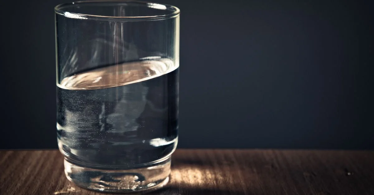 Un verre d'eau transparent posé sur une table en bois contre un fond sombre.
