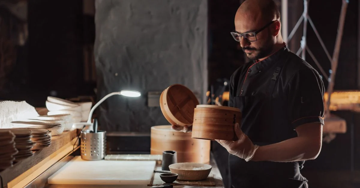 Un chef prépare habilement des dim sum dans un cuiseur à vapeur en bambou traditionnel dans une cuisine de restaurant.