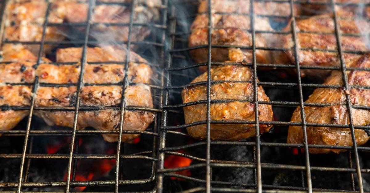 Gros plan sur de la viande juteuse en train de griller sur un barbecue au charbon, produisant de délicieuses saveurs fumées.