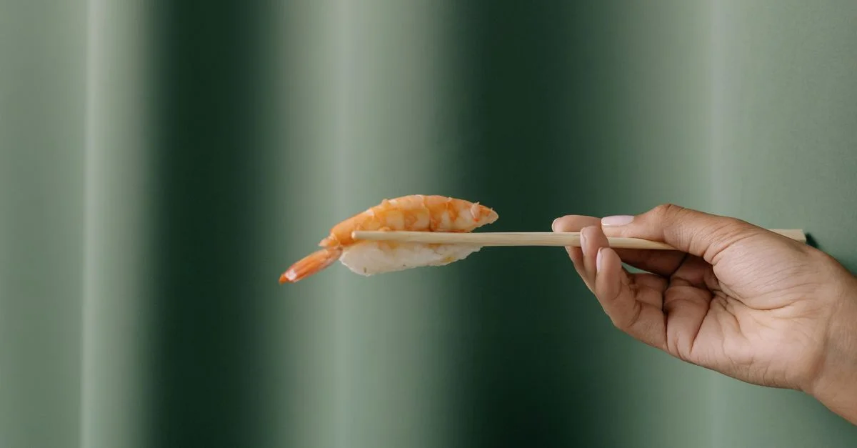 Une main tenant un sushi avec des baguettes sur un fond vert. Capture élégante et minimaliste de la cuisine japonaise.
