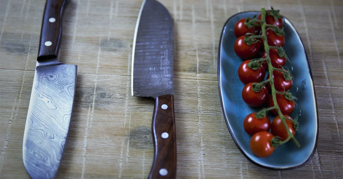 Deux couteaux de cuisine professionnels aux côtés de tomates cerises fraîches sur une table rustique.