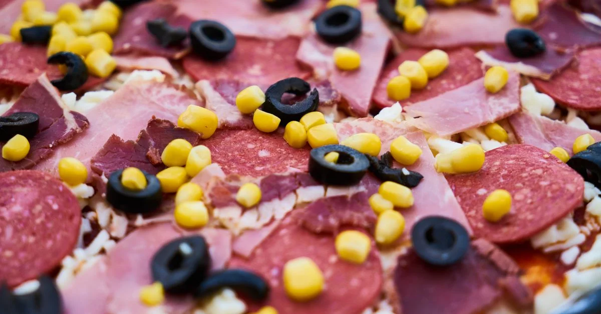 Pizza à la viande fraîchement préparée, garnie d'olives, de maïs et de fromage.