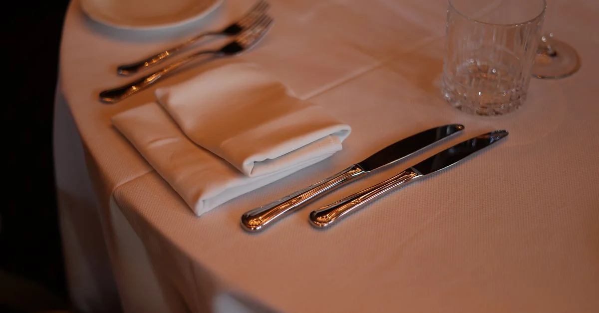 Gros plan d'une table de restaurant avec des couverts, des serviettes et un verre sous un éclairage chaleureux.