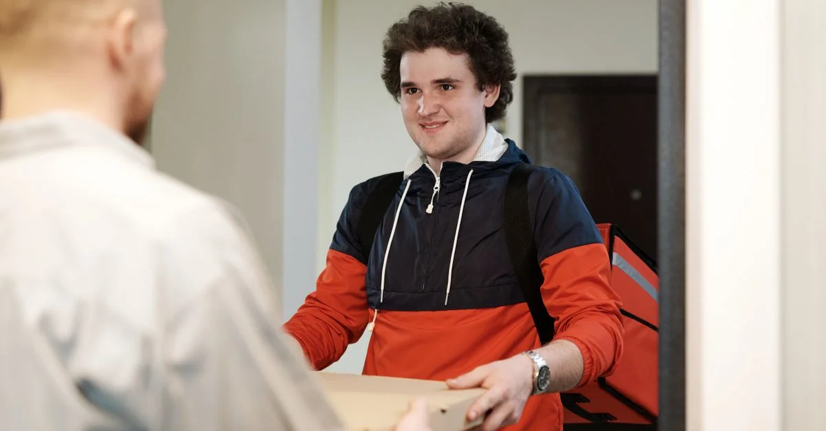 Un livreur de pizza en tenue décontractée livre une boîte de pizza à un client à l'intérieur, souriant