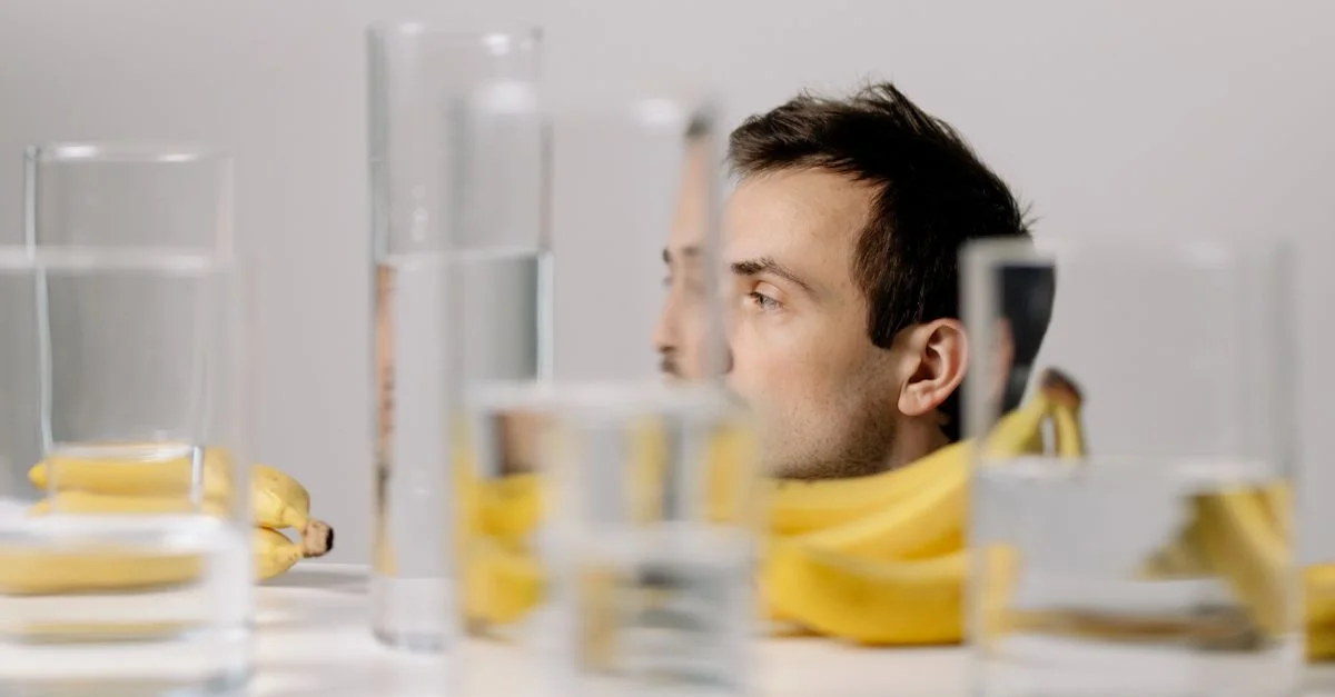 Portrait artistique d'un homme entouré de verres et de bananes, créant des réflexions uniques.