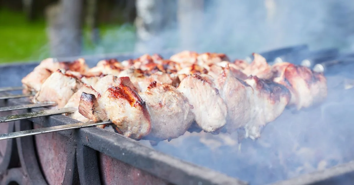 Gros plan sur de succulentes brochettes de viande grillée dégageant de la fumée sur un barbecue au charbon de bois en extérieur.