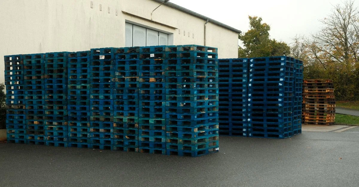 Énorme empilement de palettes en bois bleues devant un bâtiment, prêtes au transport.