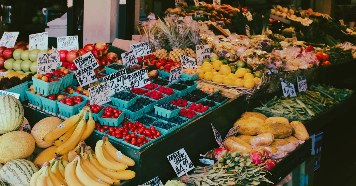 Stand de marché coloré de fruits et légumes affichant une variété de produits frais avec des étiquettes de prix visibles.