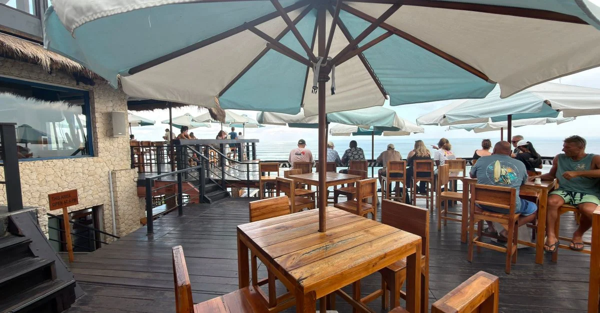 Restaurant en bord de mer avec tables en bois et parasols offrant une vue sur l'océan.