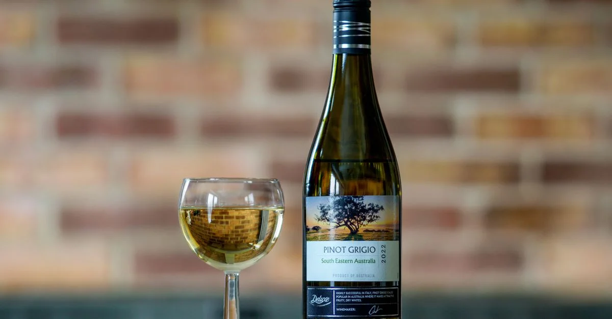 Affichage classique d'une bouteille de vin Pinot Grigio et d'un verre sur une table en bois avec un fond en brique.