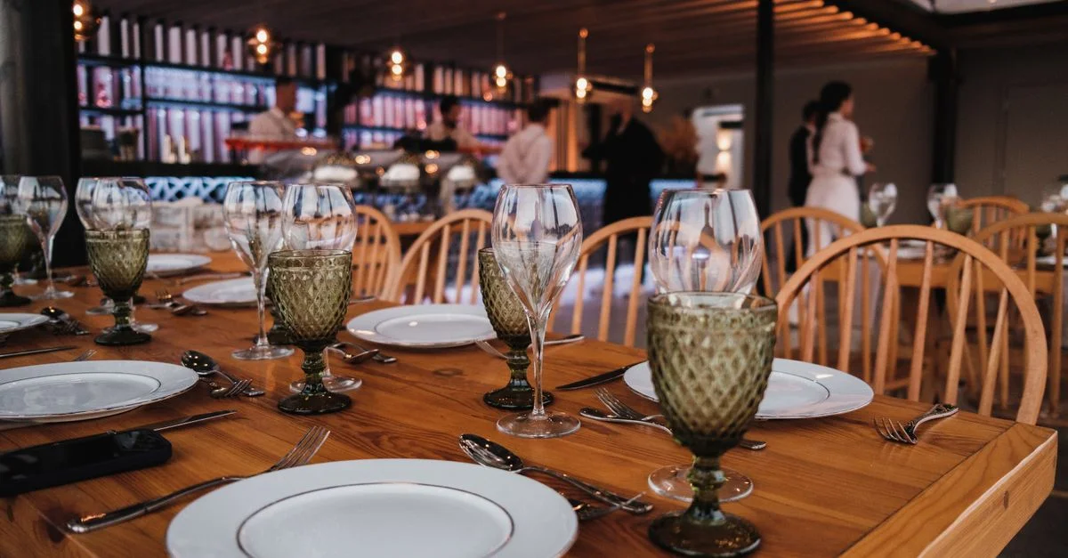 Une table de restaurant joliment dressée avec des verres, des assiettes et des couverts dans une ambiance chaleureuse.
