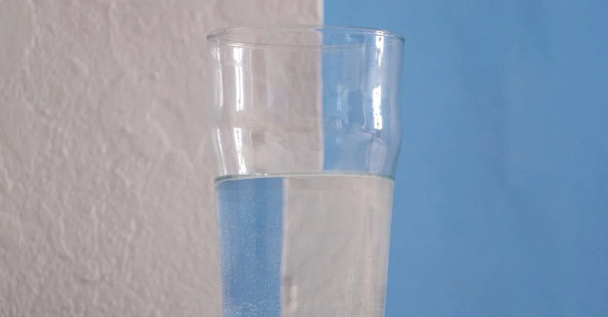 Une photo minimaliste d'un verre d'eau sur une table avec un fond bleu et blanc.