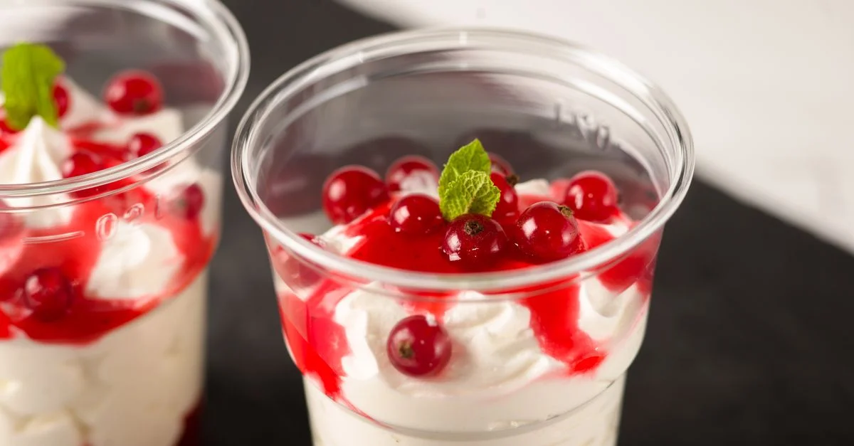 Gros plan sur un dessert coloré aux fruits rouges et à la crème, agrémenté d'une feuille de menthe, servi dans des gobelets en plastique.