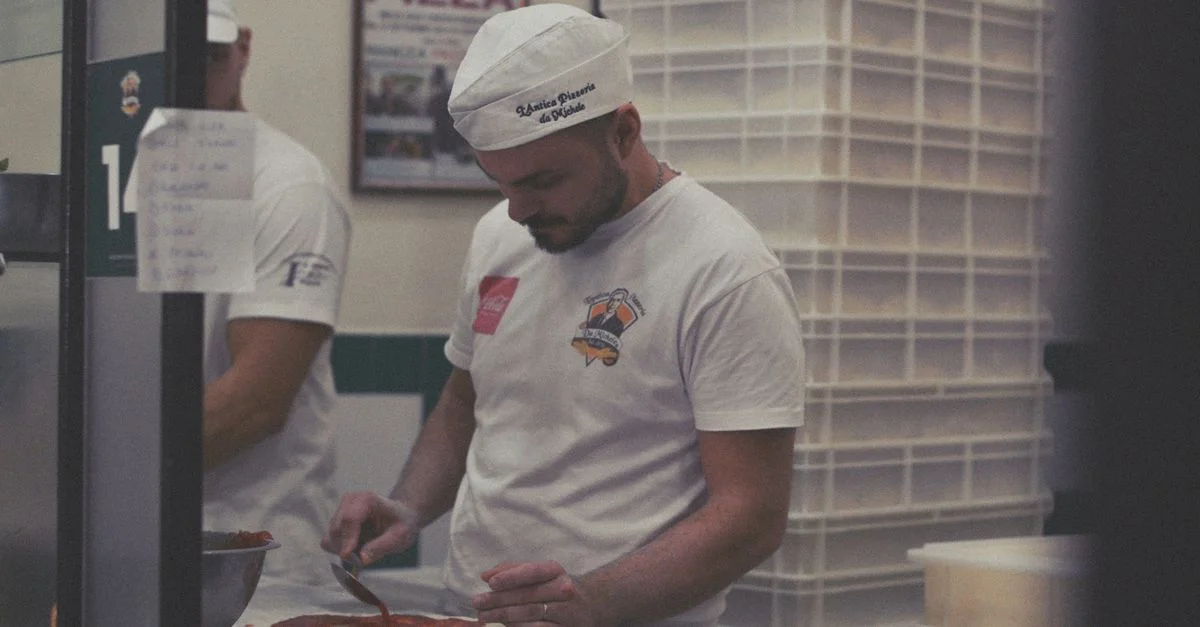 Chef pizzaiolo étalant la sauce sur la pâte dans la cuisine d'un restaurant à Naples.