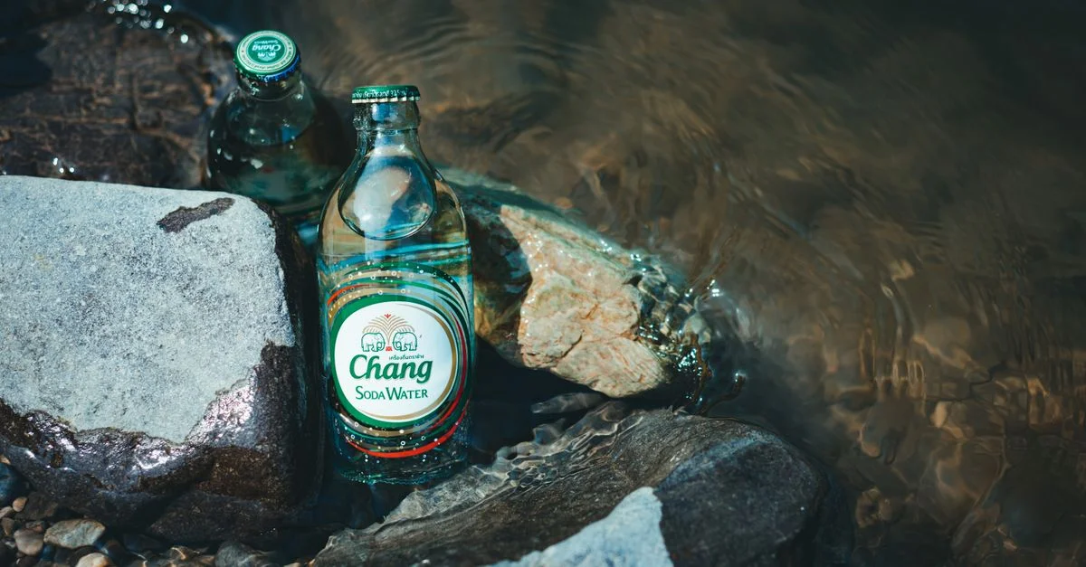Bouteilles en verre de soda Chang placées sur des rochers de rivière avec de l'eau qui coule, créant une scène rafraîchissante.